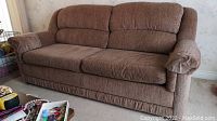 Front angle view of the brown Sklar Peppler sofa bed showing cushions and armrests, placed on carpet.