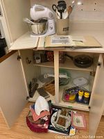 Overview of the contents on counter and inside lower cabinet, showing various kitchen tools, linens, and gadgets.
