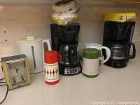 Various small kitchen appliances including coffee makers, kettles, insulated thermoses and beverage containers, and a vintage oven clock.