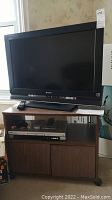 Wide shot showing Sony Bravia 32 inch LCD TV on wood TV stand, JVC DVD/CD player visible on glass shelf.