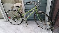 Side view of green Supercycle cruiser style road bike with 18 inch frame, chrome fenders, white padded seat, tires on snow ground.