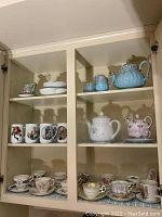 Photos of multiple tea cups and saucers, mugs, and tea pot sets displayed in cabinet, showing variety of patterns and styles.