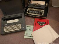 Two electric typewriters placed on a floor surface, with the Smith Corona SL470 typewriter including a user manual, carbon paper, and tracing paper placed in front.