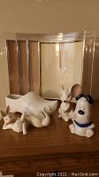White ceramic figurines including dog, rabbit, swan, and mouse, ceramic shoe, and four curved 8x10 photo frames on wooden surface