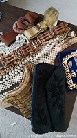 Photo displaying two beaded evening purses, pearl-like bead necklaces, multiple metal and wooden linked belts, and gold-tone costume jewellery items spread on a table.