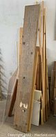 Various lengths of wood boards leaning against a wall including a large 2x10 or 2x12 board, and shorter 2x4 boards.