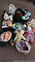 Overall view of bags filled with yarn skeins, several handmade dolls, and pattern books scattered around