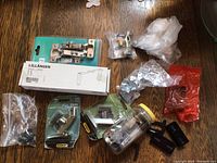 Photo showing assorted hardware including LILLÄNGEN cabinet hinge in box, Stanley shelf bracket in packaging, loose bags and jar filled with various screws, hinges, and metal fasteners.