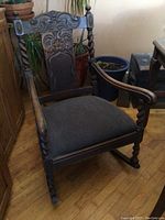 Front angled view of oak rocking chair showing barley twist arms, legs, and carved backrest with green tweed upholstery.