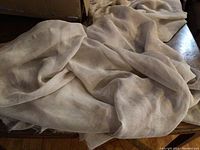 Beige sheer fabric crumpled and spread on a surface showing texture and color.