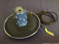 Blue ceramic round electric fountain with cord and plug visible, showing the full base and central textured column.