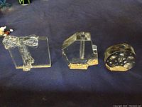 Three clear glass items shown on a dark cloth background: a candle holder with a bow, a geometric shaped egg holder, and a round shaped egg holder with indentations.