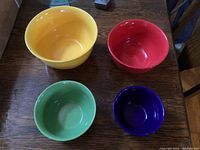 All four nesting mixing bowls displayed on a wooden table, showing their relative sizes and colors: yellow, red, green, blue.