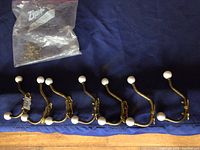 Seven double brass hooks with white porcelain ball ends arranged in a row on a blue surface with a package of mounting screws.