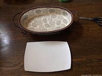 Top view of the oval ceramic dish on a wooden surface, showing black and white floral pattern and brown rim.