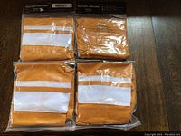 Four pairs of gold and white stripe hockey socks in sealed packaging lying on wooden floor.