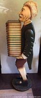 Side view of large wooden butler figure holding book stack storage case showing detailed facial features and elegant pose.