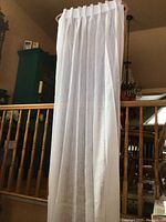 Full view of one sheer white drapery panel hung on a rod with pleated header.