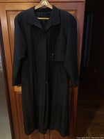 Front view of the vintage black long back coat hanging, showing full length, collar and button front closure.