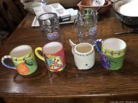 Photo showing three ceramic mugs and two glass beer steins on a wooden table.