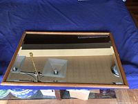Top view of the oak framed mirror laying flat on a blue cloth, showing clear mirror glass and wood frame