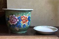 Front view of ceramic flower pot with colorful floral decoration beside separate base with floral rim design.