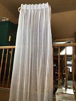 Full view of one white sheer drapery panel held up vertically showing length and width, prehooked heading.