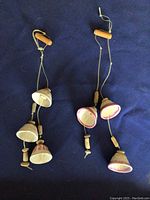 Three handmade South American hanging art pieces laid flat on a dark surface, showing bell or gourd shaped elements with wooden beads and painted details.