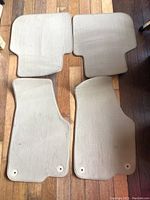 Top view of four tan VW Passat floor mats showing front mats with retention holes and lightly soiled fabric padding.