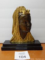 Front view of the sculpture bust showing the veiled woman with intricately patterned gold veil and rose ornament, mounted on black marble base.