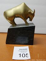 Full view of bull sculpture on marble base atop wooden surface.