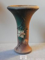 Front view showing the full height of the terracotta vase with magnolia flowers sculpted on the body. The flared rim is visible at the top.