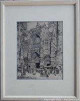Full view of the framed etching 'The Year-Mart in Rouen' showing the architectural scene with market activity in grayscale, light wood frame and cream matting.