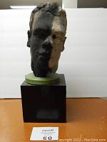 Front view of painted hard clay bust sculpture on black pedestal showing contrasting paint on face and details of the facial features.