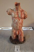 Full view of painted glazed hard clay sculpture of nude male torso kneeling on base, showing front and right side, placed on neutral background with MaxSold lot card.