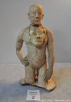 Front view of signed clay bust sculpture of nude male figure with mask around neck.