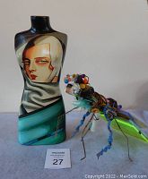 Photo of both ceramic painted woman vase and handmade grasshopper sculpture together showing scale and appearance