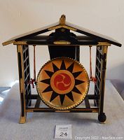 Front view of prayer drum suspended in lacquered wooden shrine-style frame with gold hardware and braided cords.