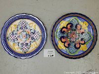 Two colorful hand painted ceramic plates side by side on floor, showing front with intricate traditional Mexican floral and geometric decoration.