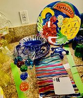 Display of assorted glassware and bowls on countertop, featuring blue glass bowls, colorful platter, several glass shot and martini glasses, and massagers.