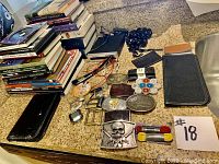 Photo showing various books stacked and multiple leather accessories including wallets, belt buckles, a keychain, bracelet, and business card holder on countertop.