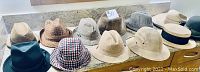 View of 12 assorted hats on countertop showing variety of styles and colors