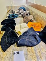 14 hats laid out on a countertop showing a variety of styles and colors including denim, black patterned, cream, plaid, and yellow embroidered hats.