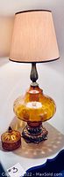 Mid-century amber glass table lamp with beige fabric shade and ornate metal base on a white surface