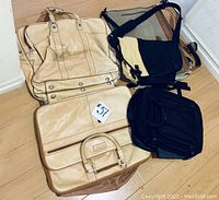 Four luggage and bags on wood floor showing two beige luggage bags, black shoulder messenger bag, and black rolling suitcase.