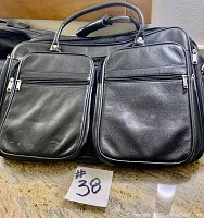 Black textured leather-like luggage bag showing front with two large zippered pockets