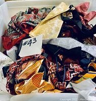 Photo of assorted men's ties, pocket squares, and scarves including paisley, striped, and geometric prints in a container.
