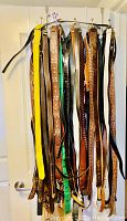 Front view of men's belts hanging on rack. Multiple belts in various colors and materials including leather and fabric. Belts vary in color: brown, black, yellow, green, and patterned. All belts have metal buckles and appear lightly used. Sizes 32, 34, 36 noted.