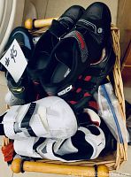 Top view of basket containing multiple pairs of cycling shoes in black, white, and mixed colors with various closure types and cleats.