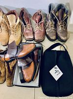 9 pairs of men's shoes arranged on the floor including boots, loafers, and casual shoes with a black bag labeled #47.